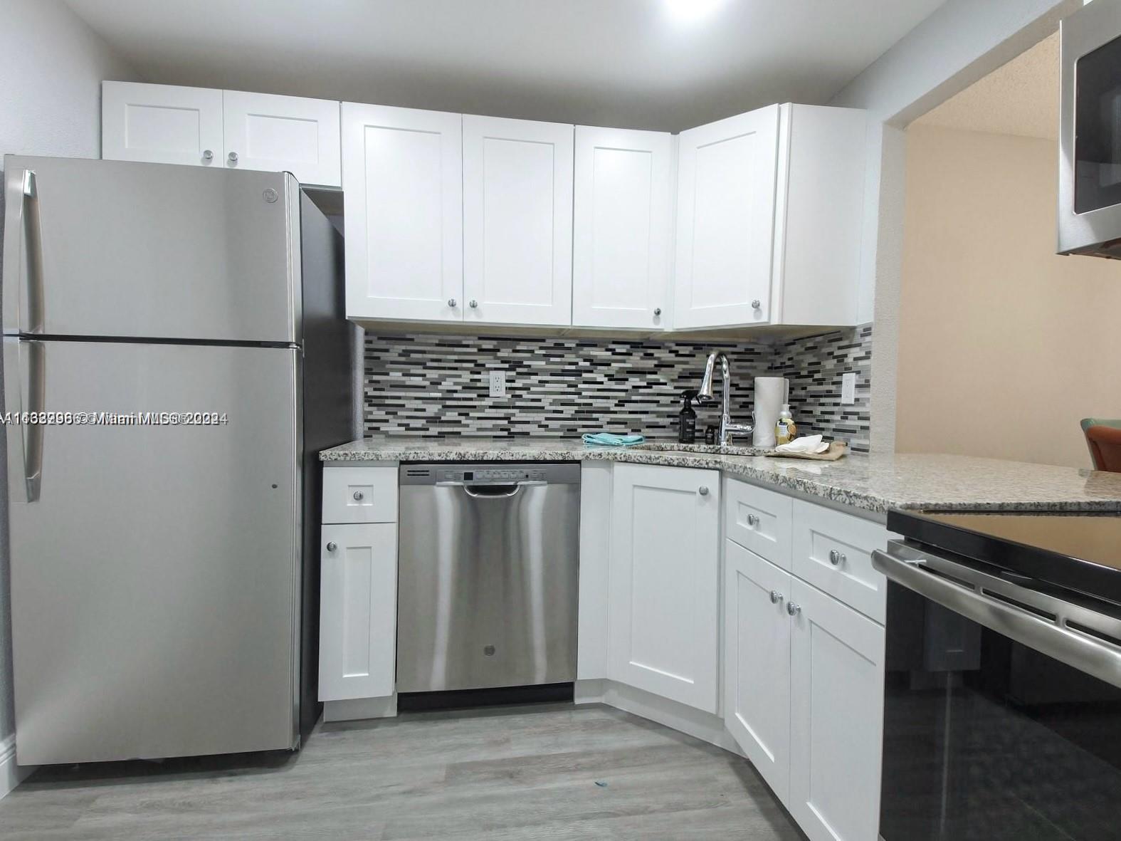 a kitchen with stainless steel appliances granite countertop a refrigerator sink and white cabinets