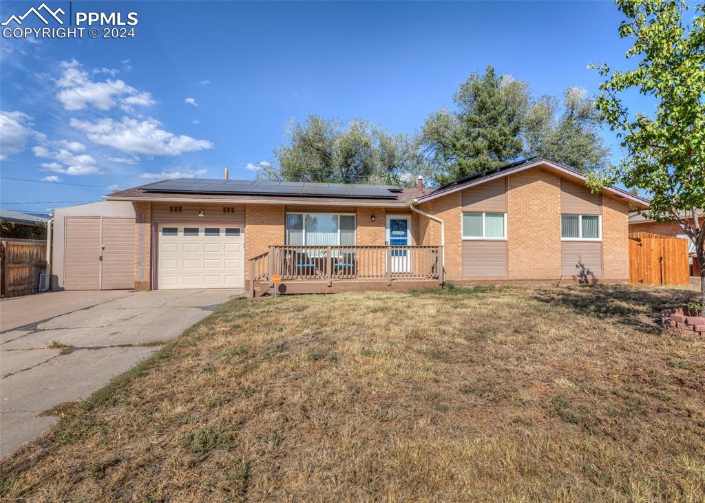 Single story home with a shed, a wooden deck, solar panels, a garage, and a front lawn