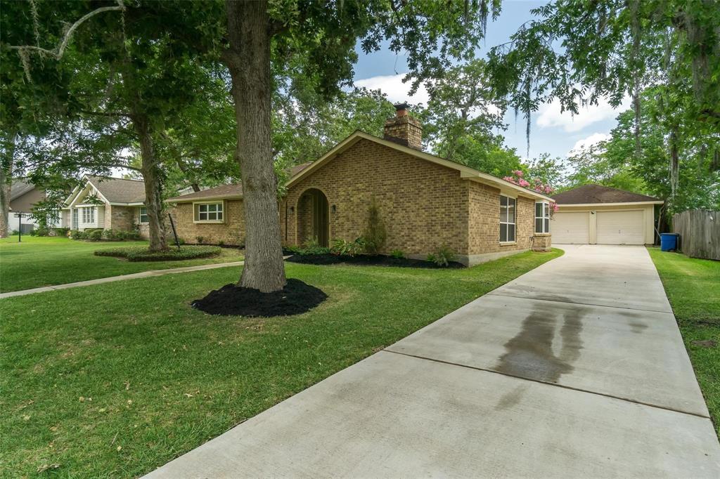 This is a single-story brick home featuring a well-maintained lawn, mature trees, and a long driveway leading to an attached two-car garage.