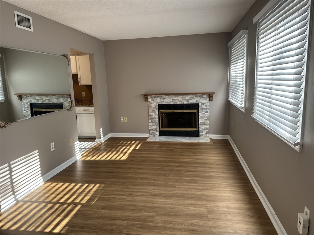 a view of an empty room with wooden floor fireplace and a window