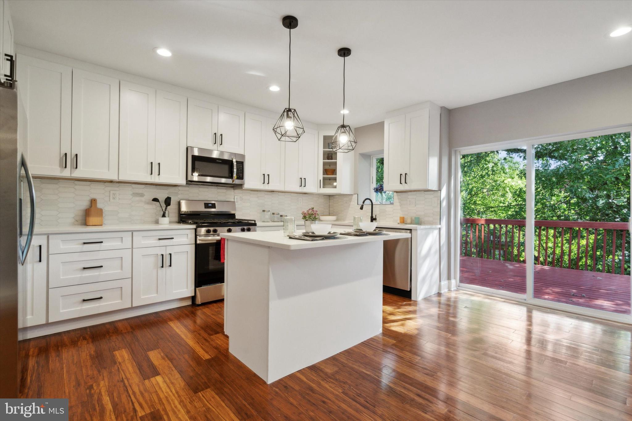 a kitchen with stainless steel appliances kitchen island granite countertop a stove a sink and white cabinets with wooden floor next to windows