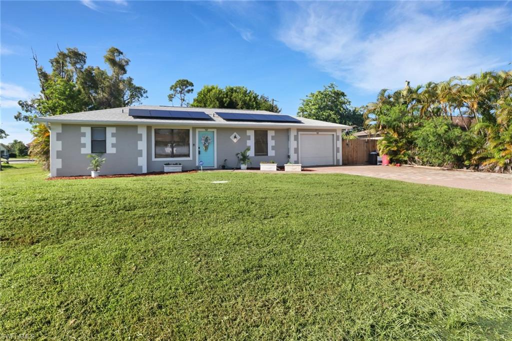 Single story home featuring a garage, solar panels, and a front yard