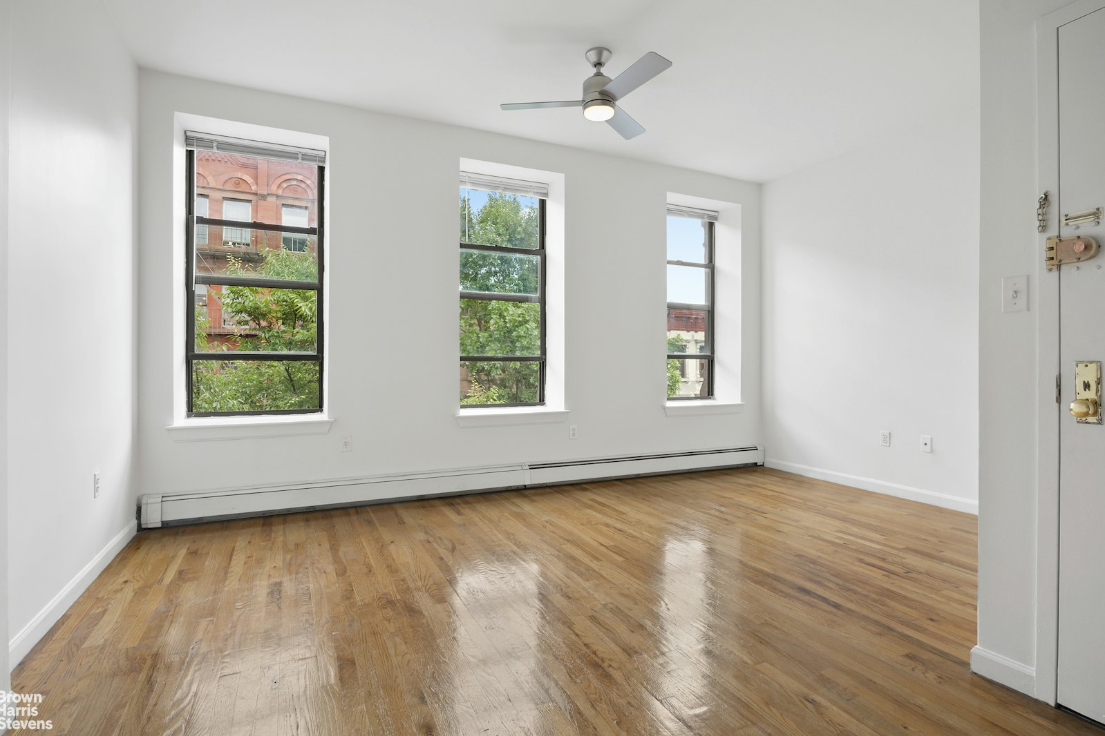 an empty room with wooden floor chandelier fan and windows