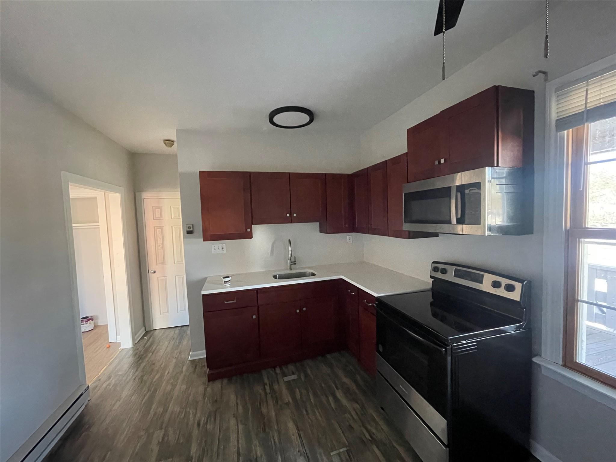 Kitchen featuring sink, dark wood-type flooring, a baseboard heating unit, and appliances with stainless steel finishes