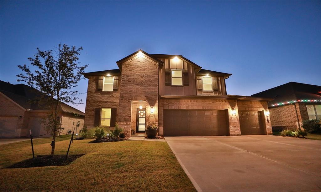 This stylish two-story brick home features a spacious driveway leading to a three-car garage. The well-lit exterior highlights a welcoming entrance and manicured lawn.