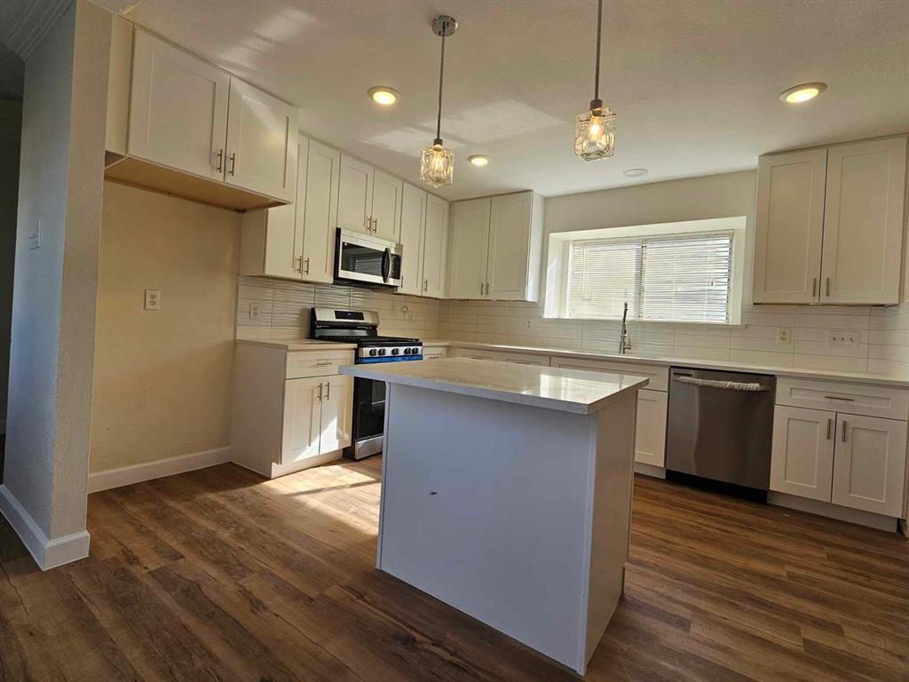 a kitchen with stainless steel appliances granite countertop a sink a stove a refrigerator cabinets and a wooden floor