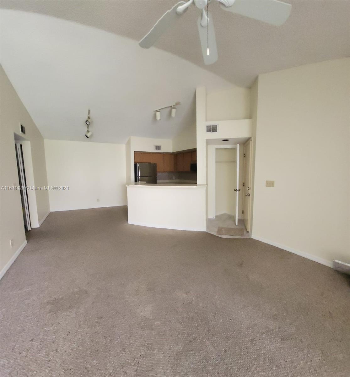 an empty room with a kitchen and a chandelier fan