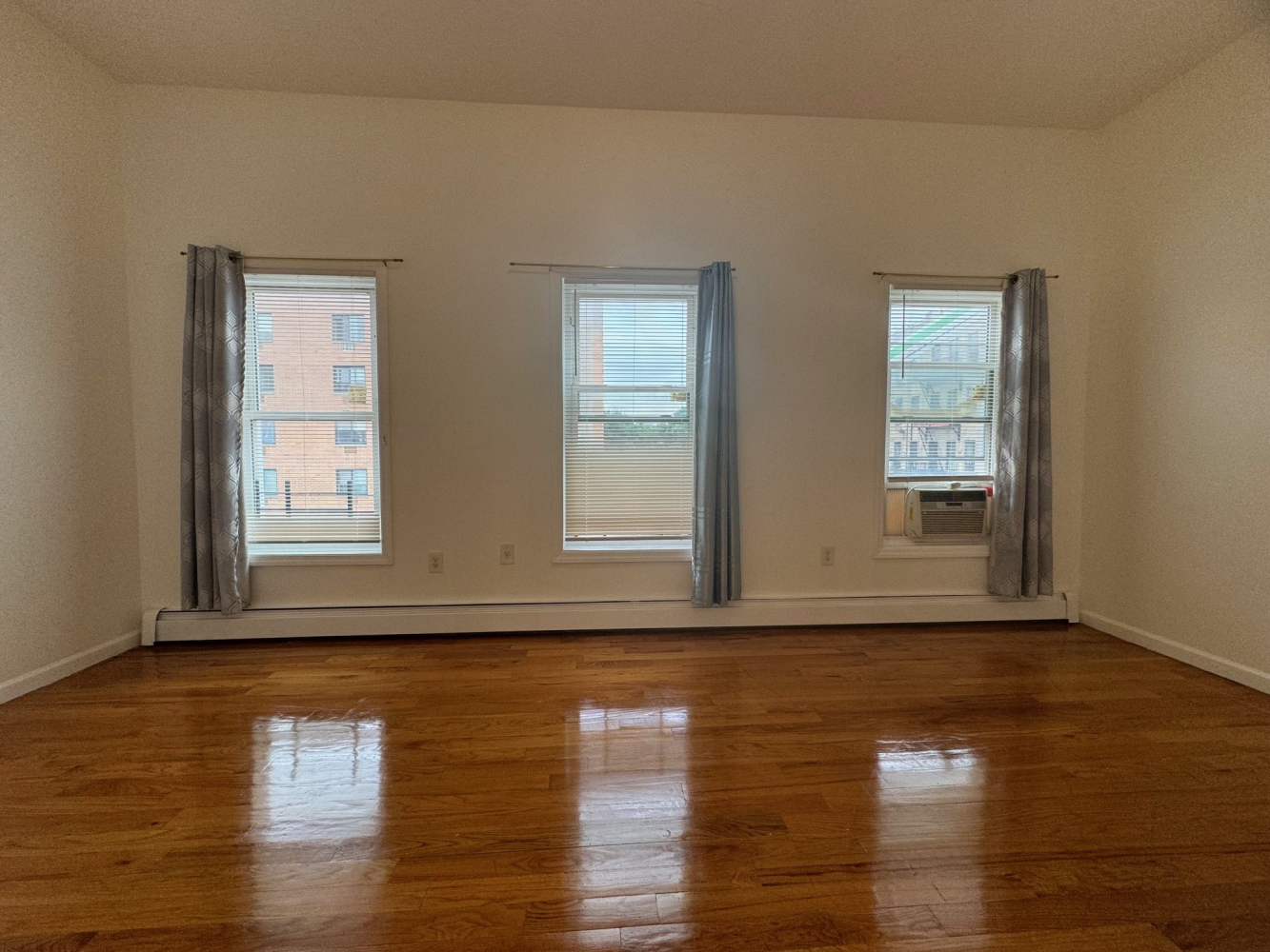 a view of an empty room with wooden floor and a window