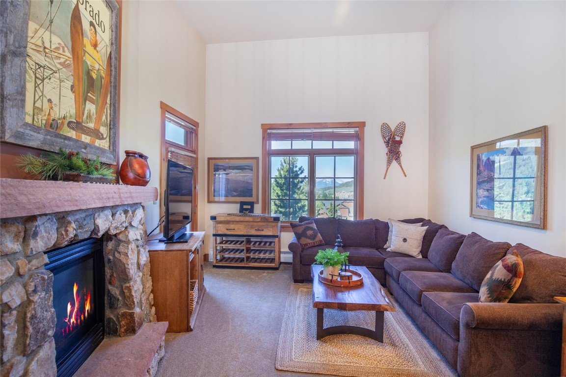 Carpeted living room with, a stone fireplace, and Vaulted ceiling