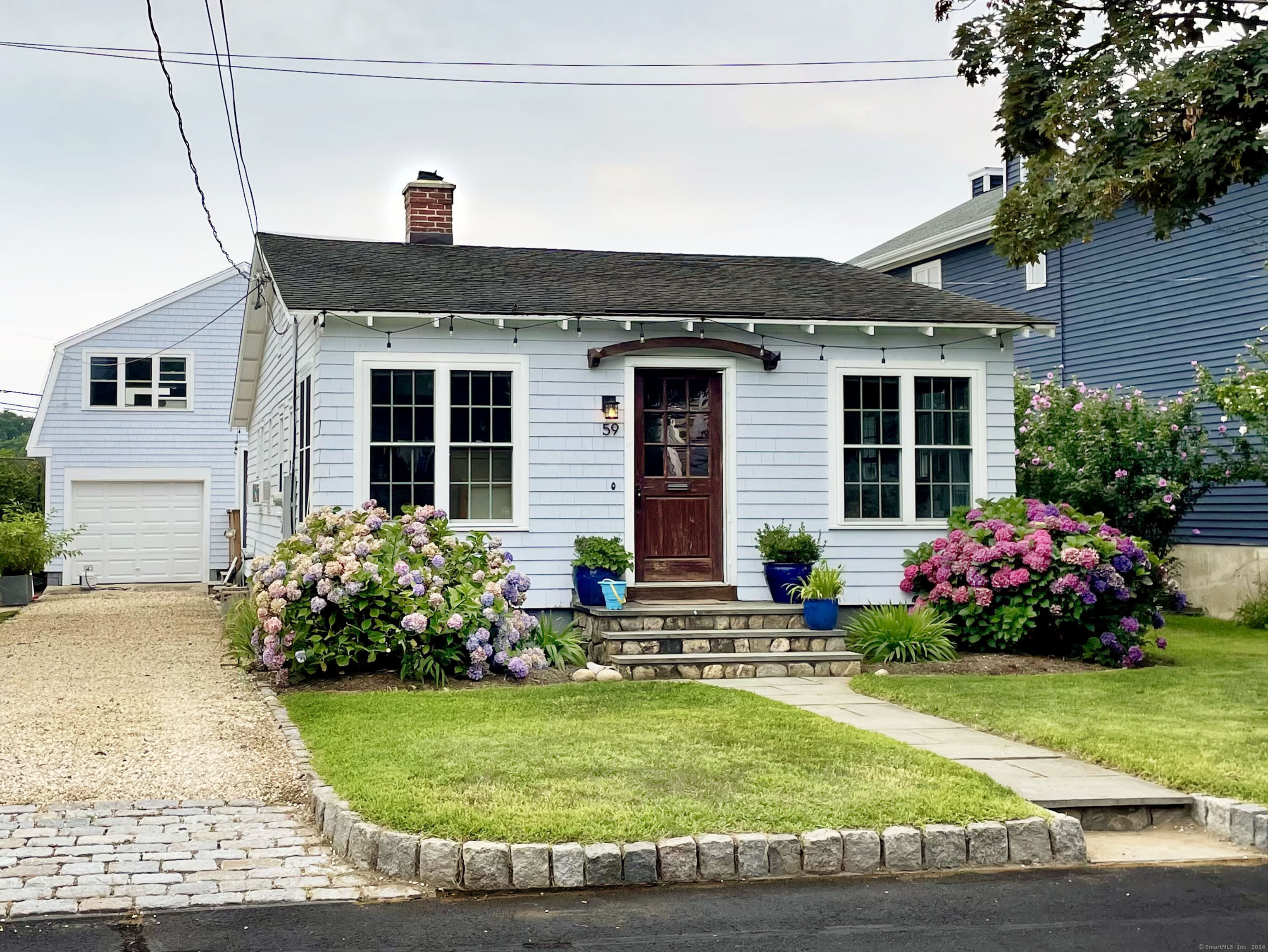 Front of cottage with grassy front yard and stone driveway, enough for 3 more cars.