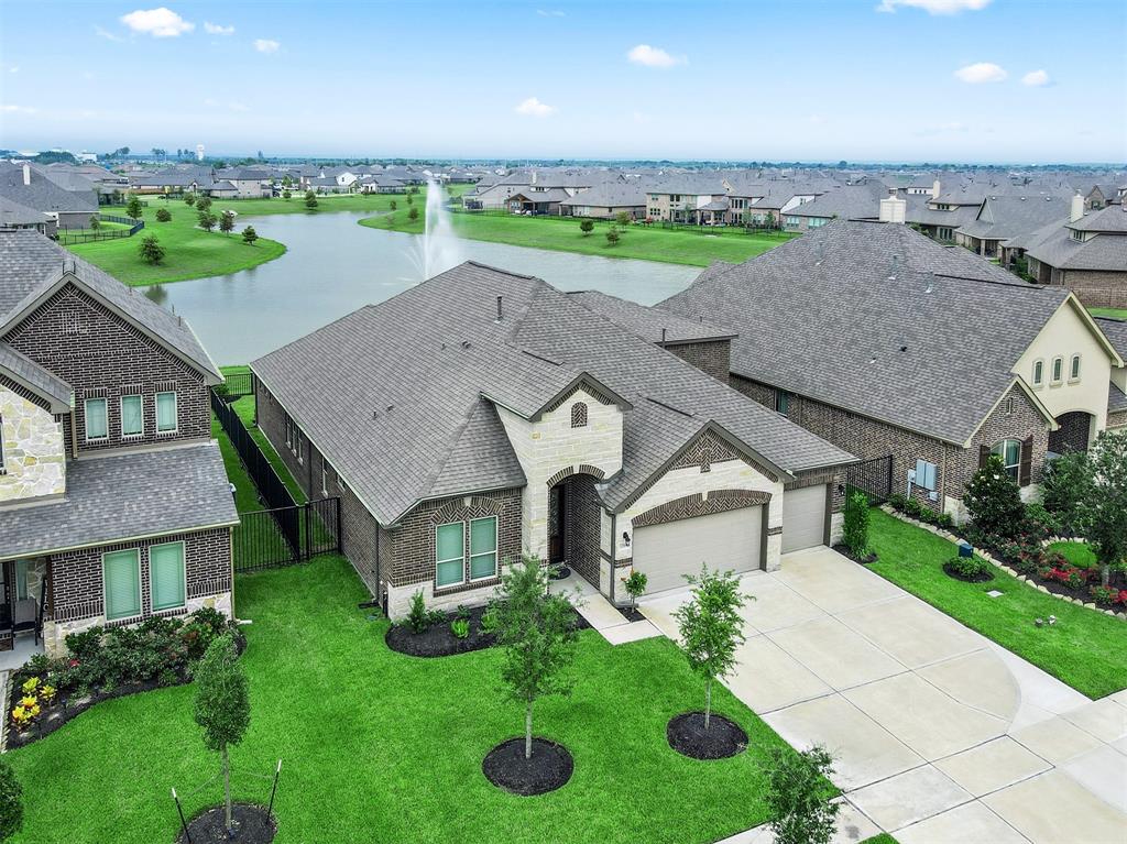 Aerial view with direct access to a community lake with a fountain feature. The property features a multi-gable roof and a three-car garage.