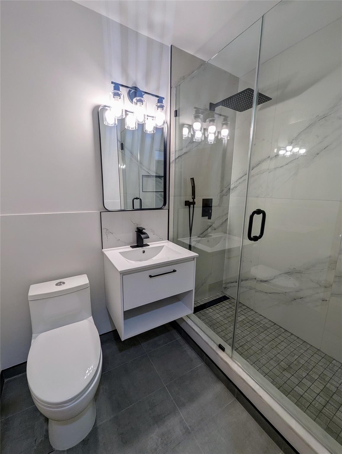 Bathroom with an enclosed shower, vanity, toilet, and tile patterned floors