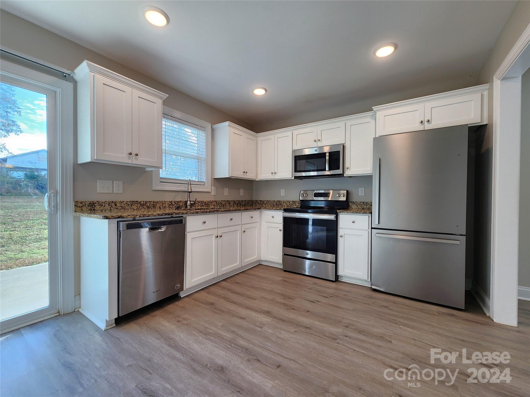 a kitchen with granite countertop a refrigerator stove top oven and cabinets