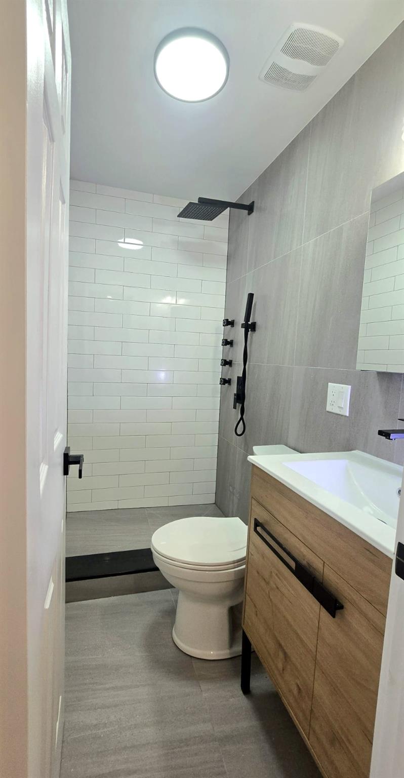 Bathroom with tiled shower, vanity, toilet, and tile walls