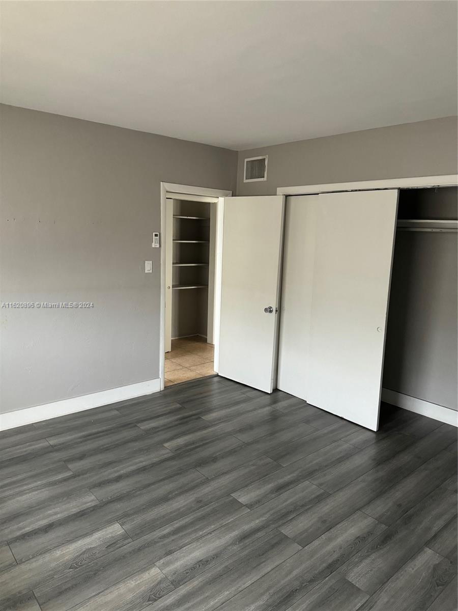 a view of an empty room with wooden floor and a refrigerator