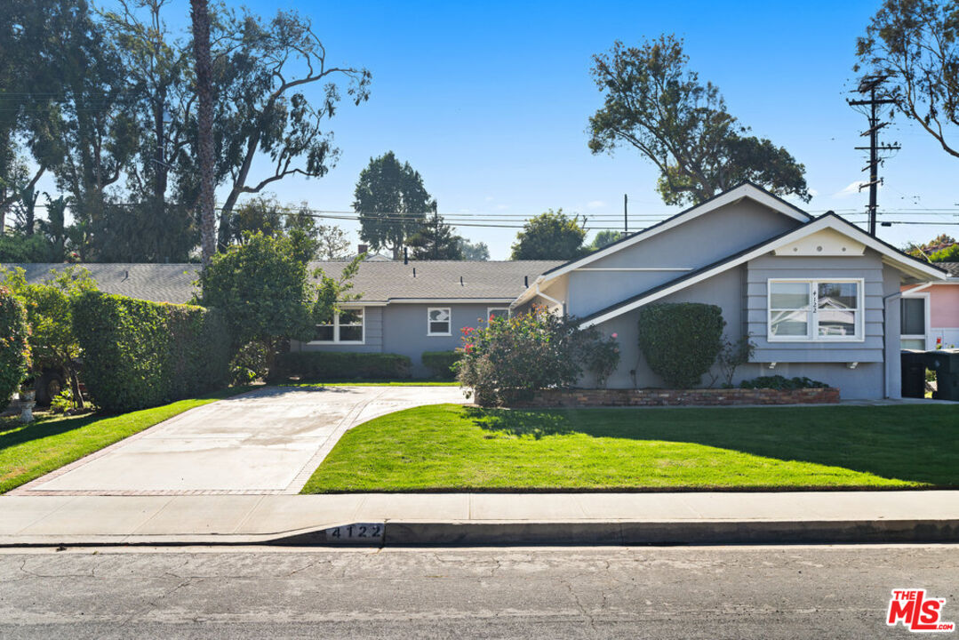 a view of a house with a small yard plants and a large tree