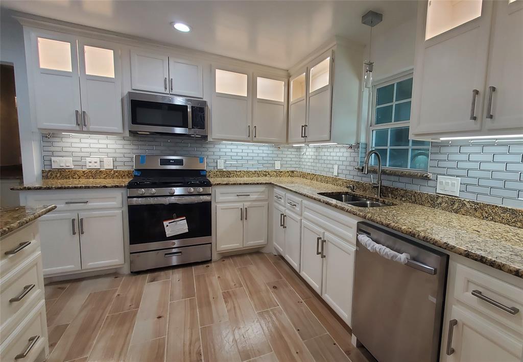 a white kitchen with granite countertop a stove top oven microwave and cabinets