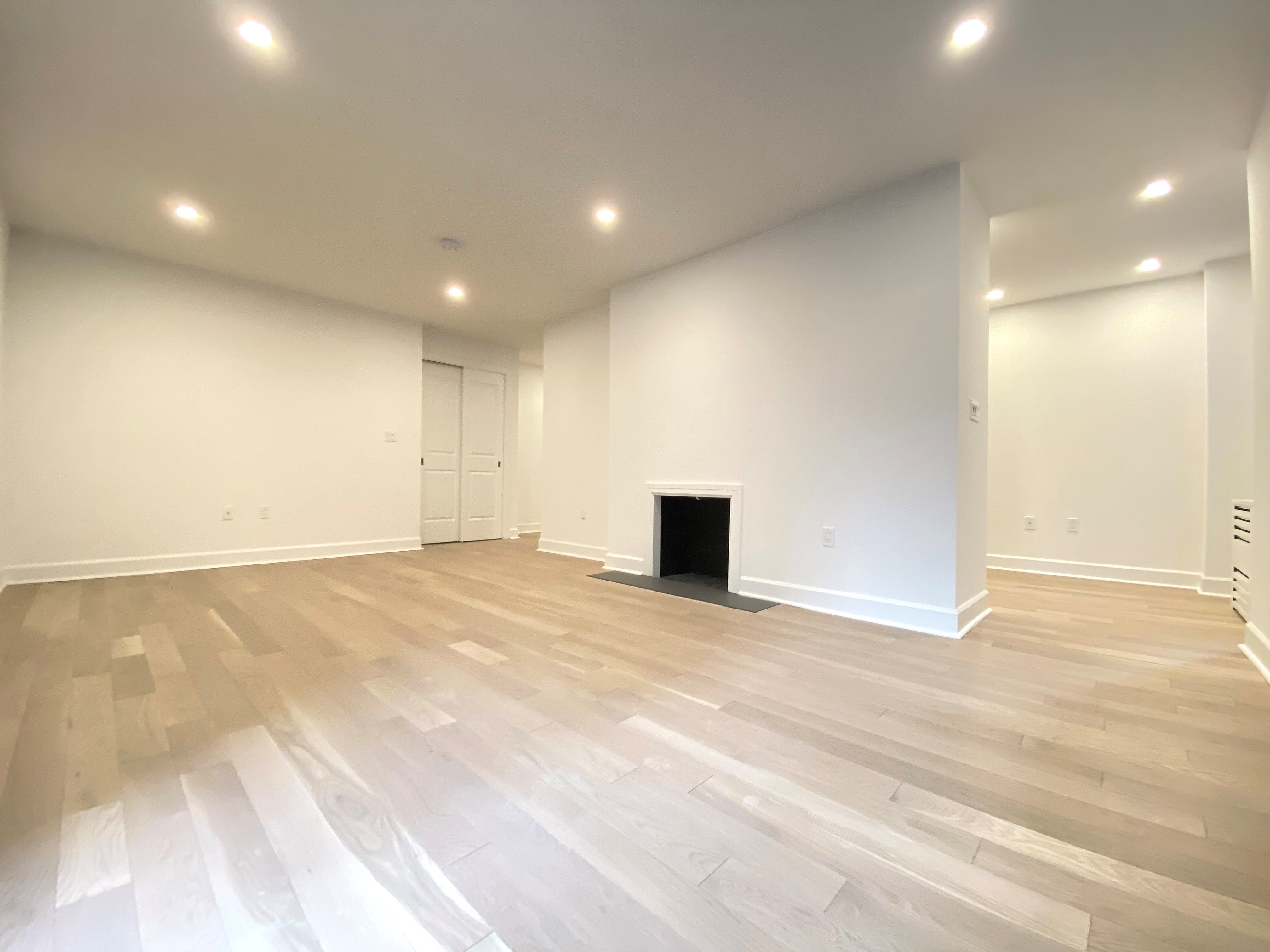 a view of an empty room with wooden floor and a kitchen space