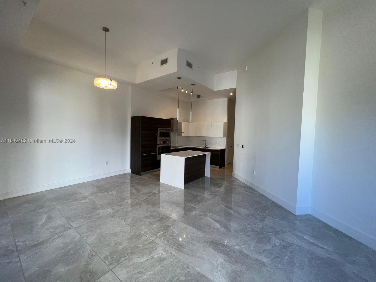 an empty room with a kitchen and a chandelier fan