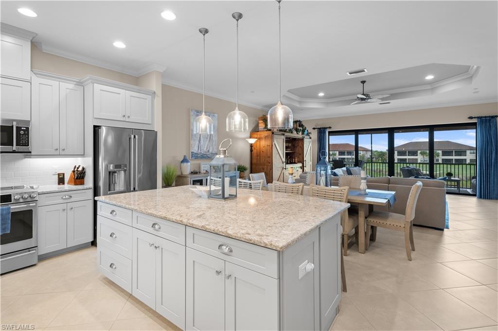 Kitchen featuring white cabinets, hanging light fixtures, appliances with stainless steel finishes, a tray ceiling, and ceiling fan