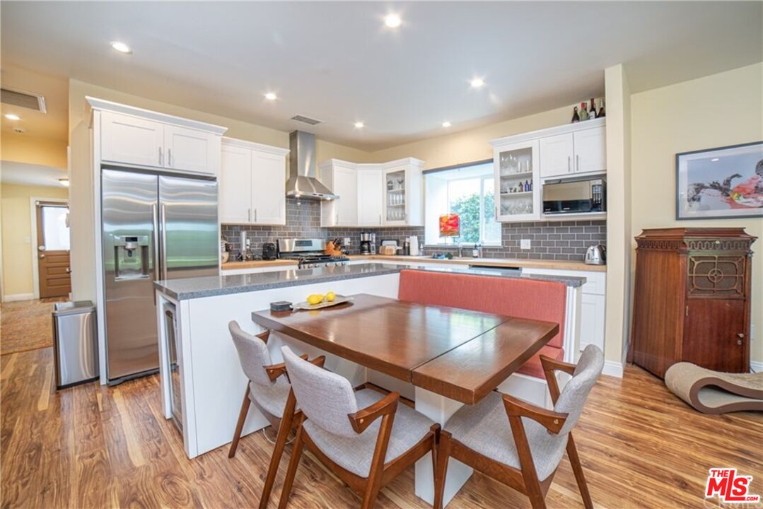 a kitchen with stainless steel appliances granite countertop a dining table chairs refrigerator and sink