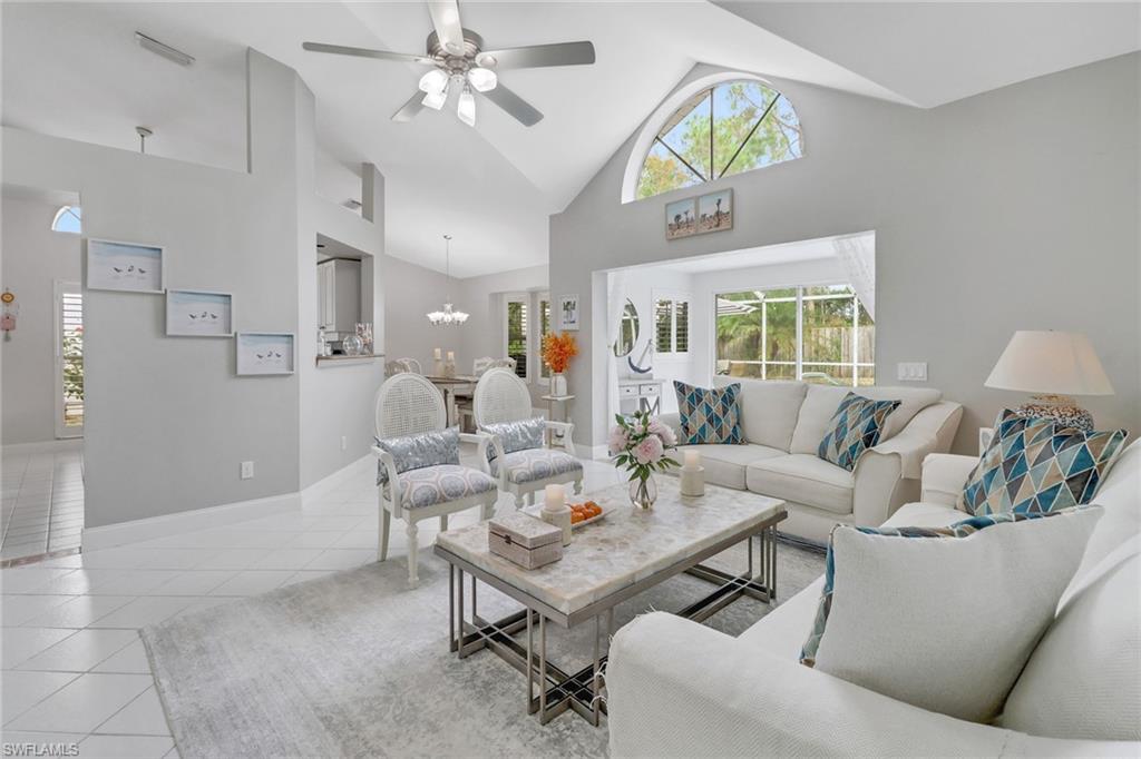 Tiled living room with high vaulted ceiling and ceiling fan with notable chandelier