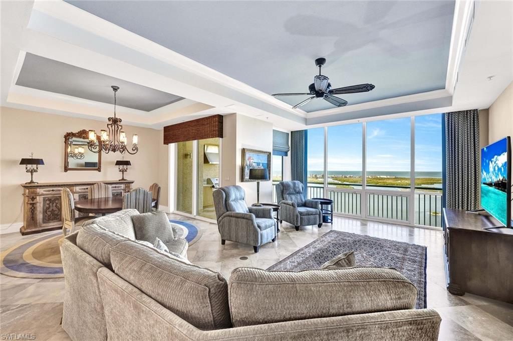 Living room featuring ceiling fan with notable chandelier and a tray ceiling