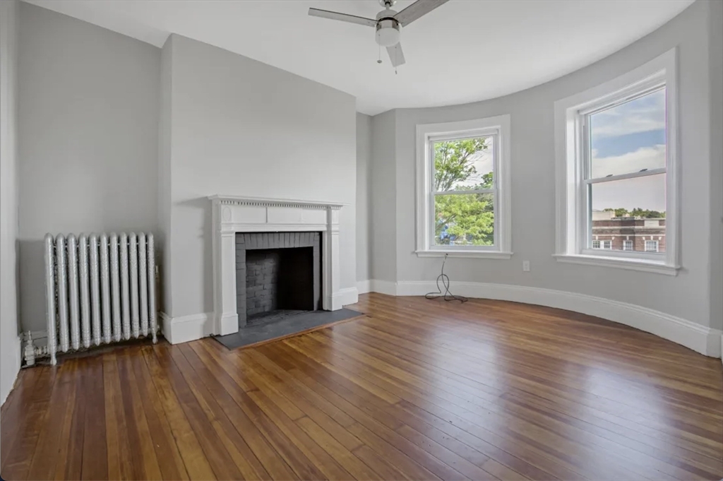 an empty room with wooden floor fireplace and windows