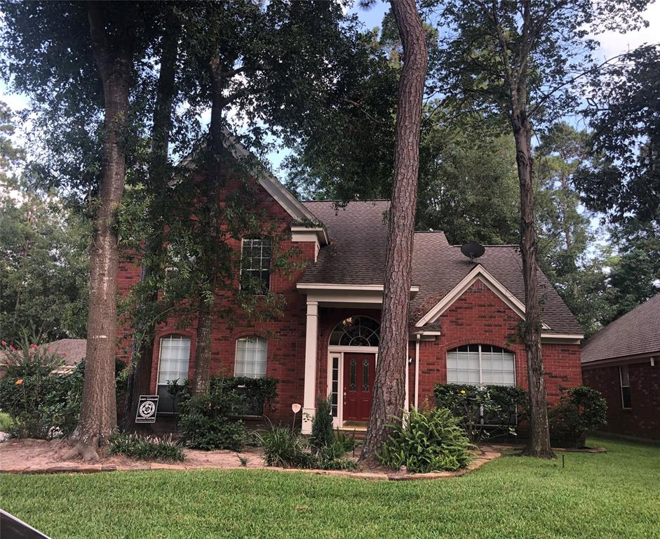 Charming two-story red brick home surrounded by mature trees, featuring a welcoming front entrance with a large arched window and well-maintained landscaping.