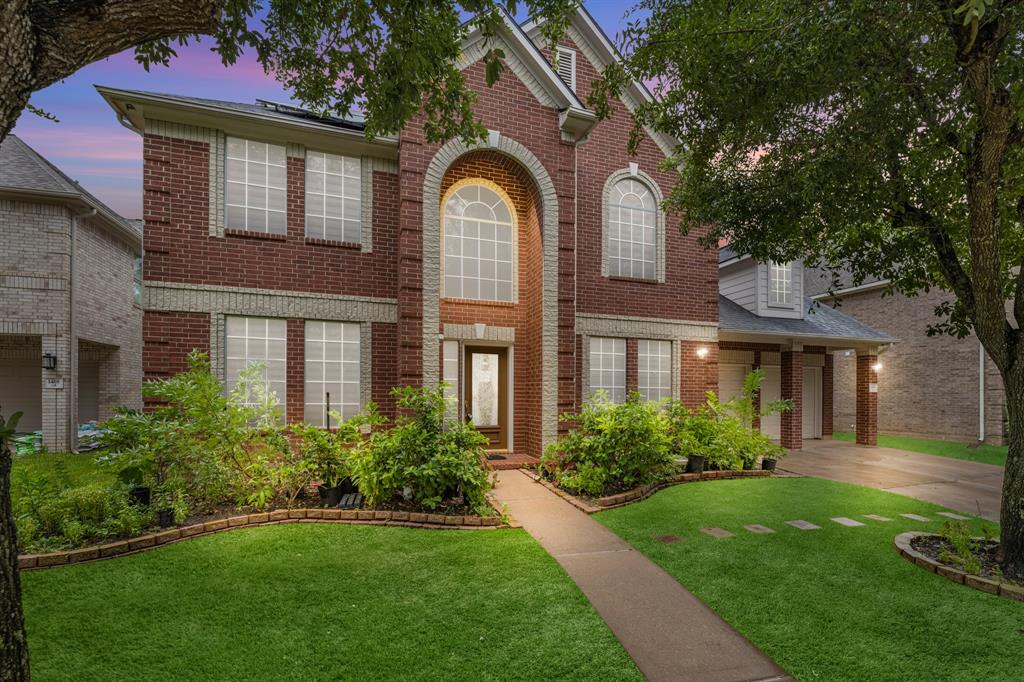 a view of a brick house with a large windows and a yard with plants and large trees