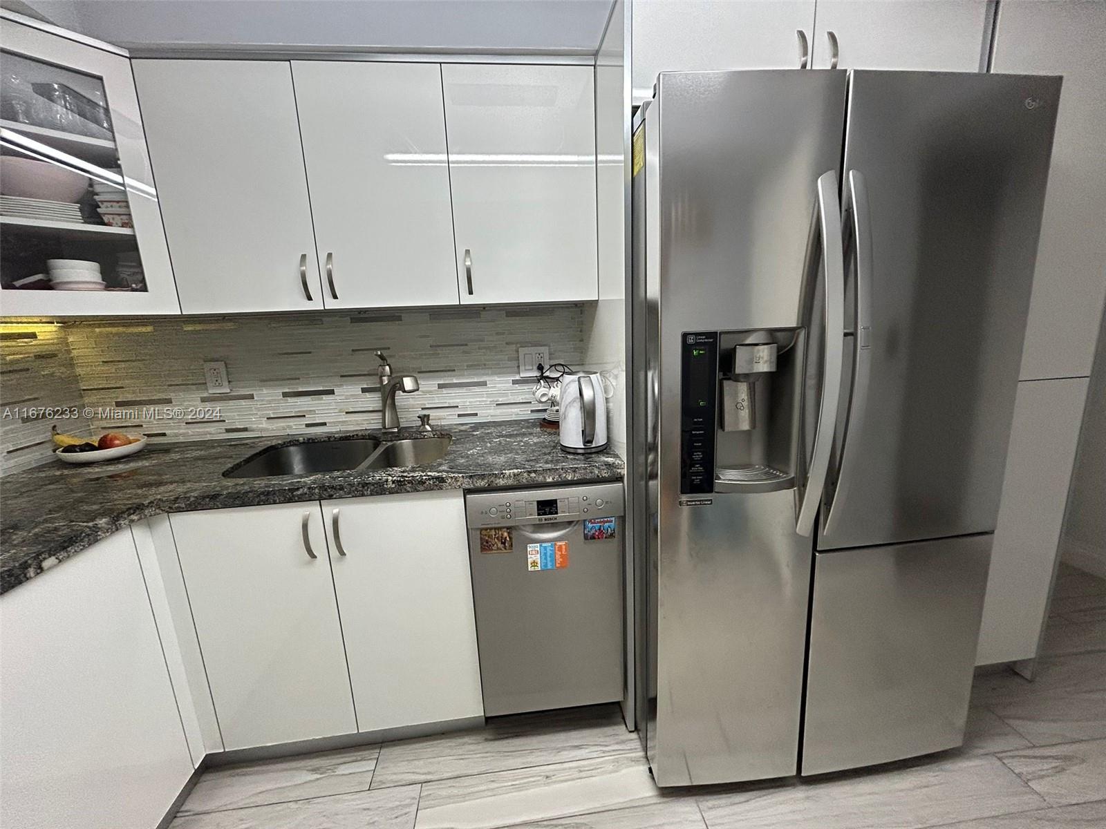 a kitchen with stainless steel appliances granite countertop a refrigerator a sink and white cabinets