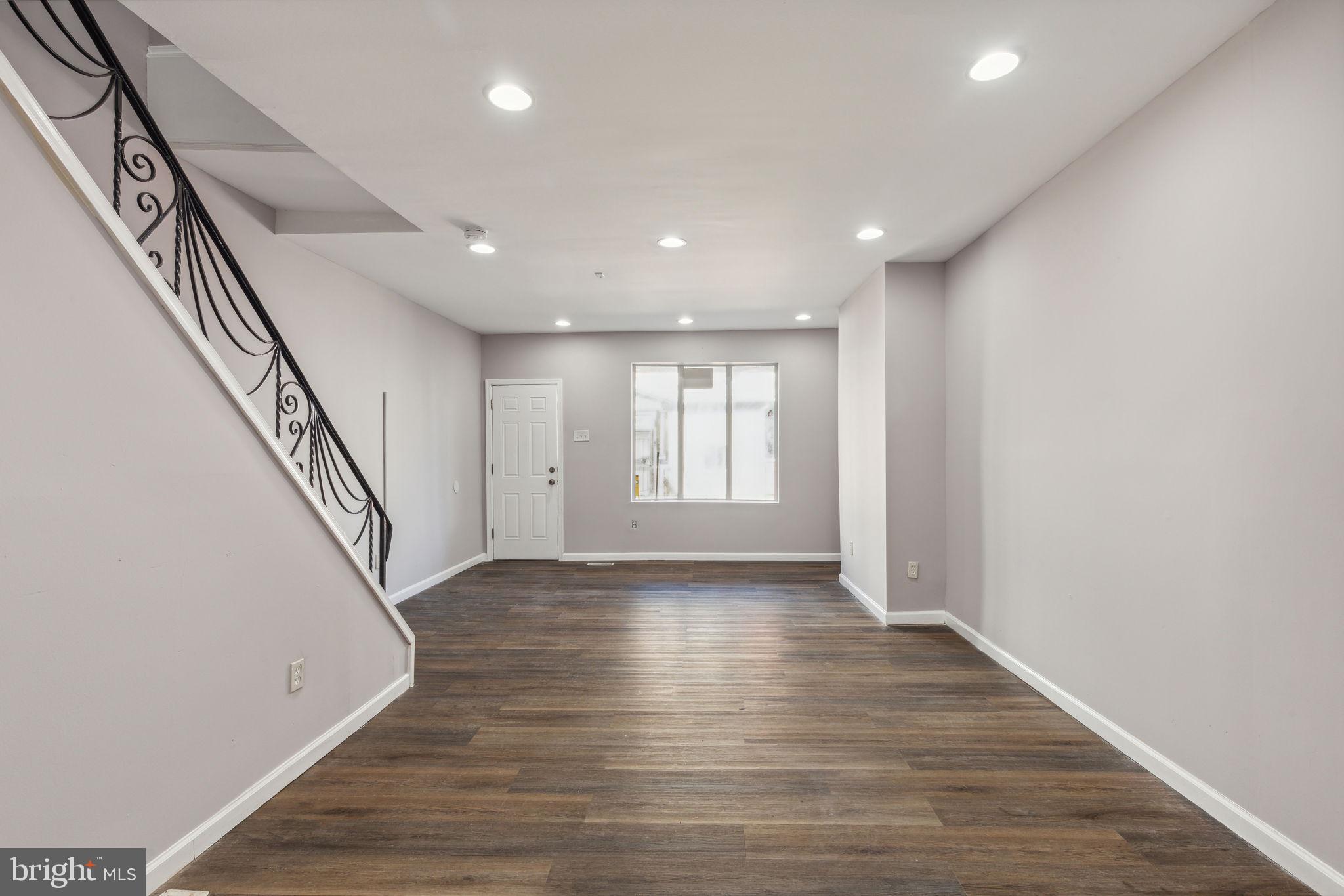 a view of an empty room with wooden floor and stairs