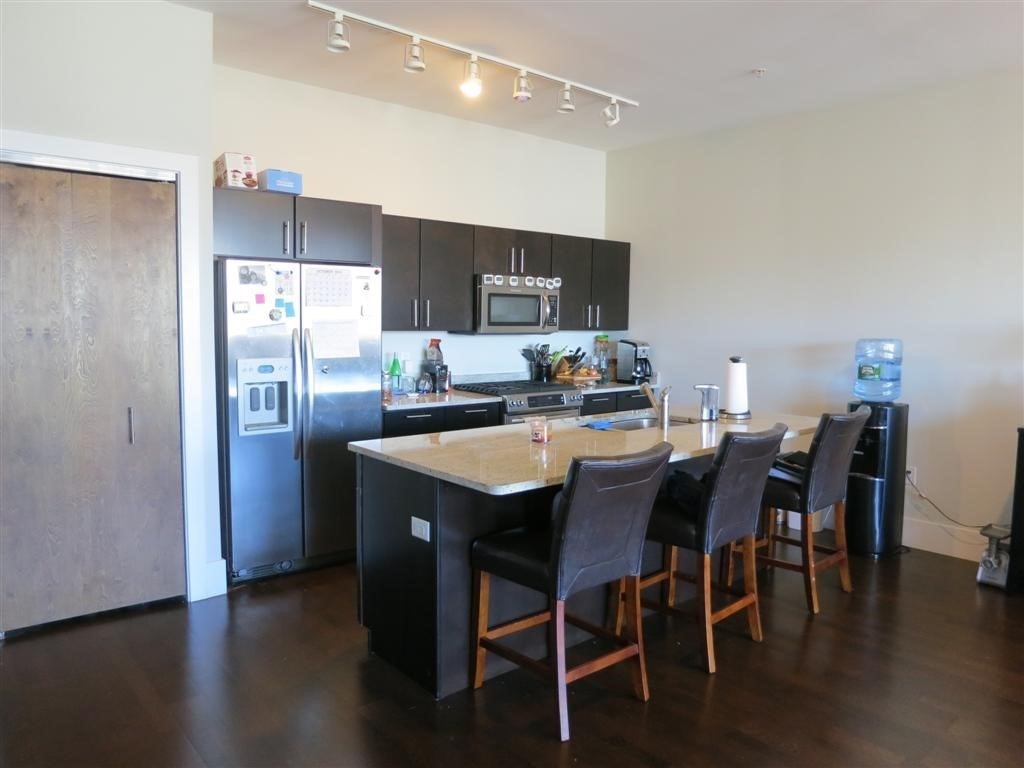 a kitchen with stainless steel appliances granite countertop a dining table chairs refrigerator sink and cabinets