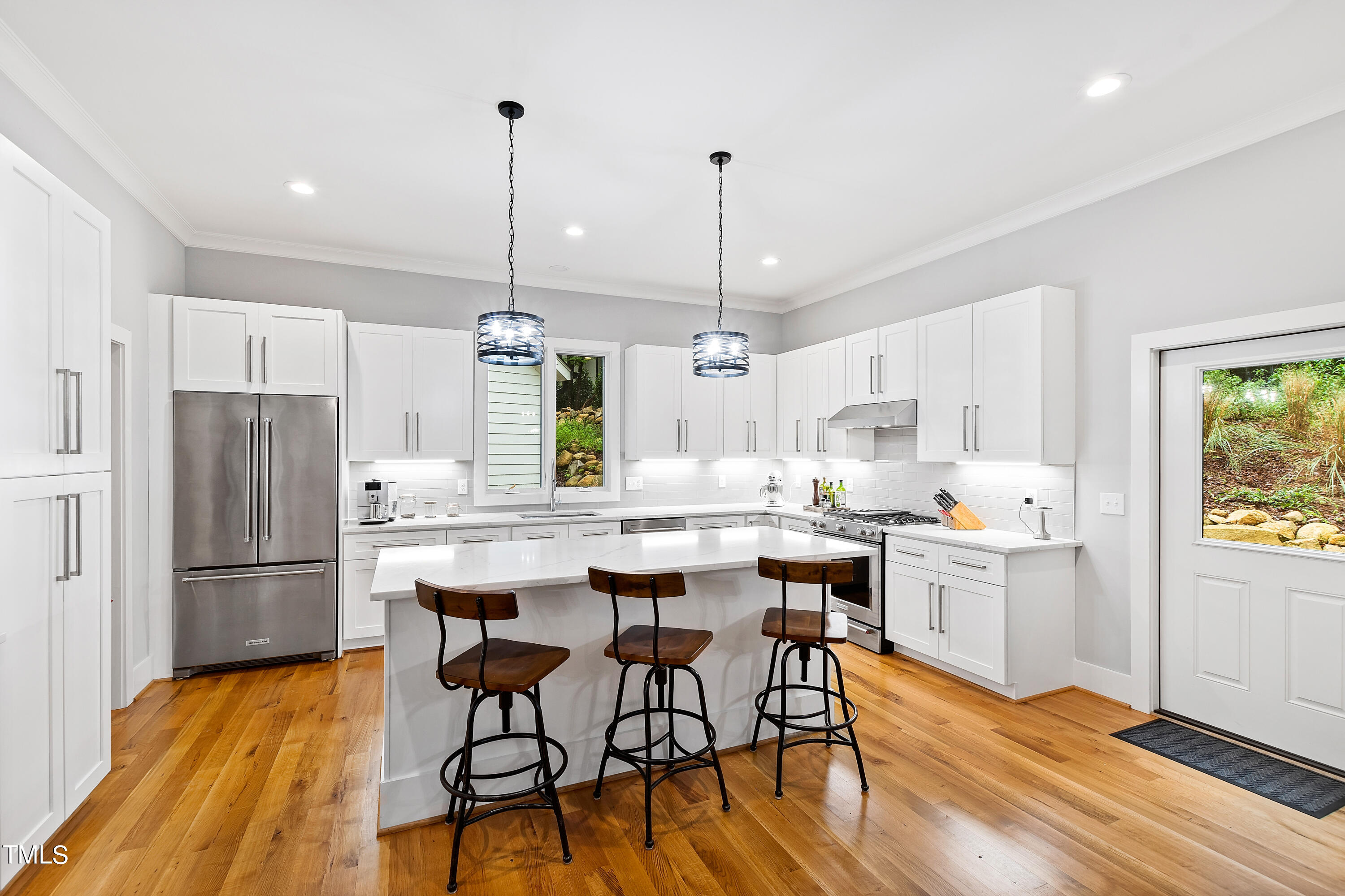 a kitchen with stainless steel appliances a dining table chairs refrigerator and sink