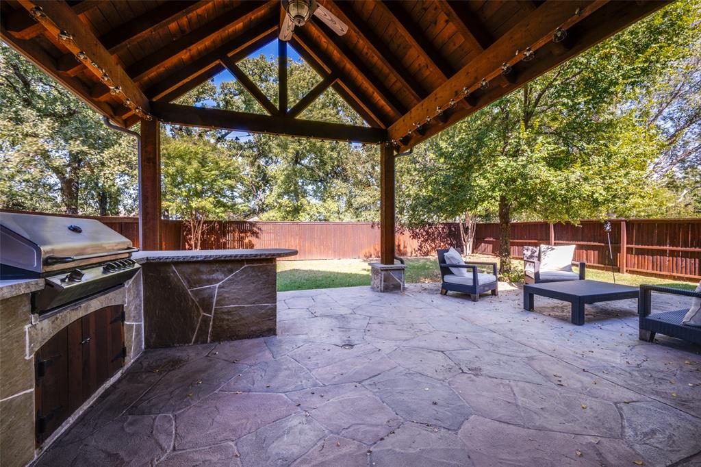 a view of a patio with table and chairs under an umbrella with a barbeque