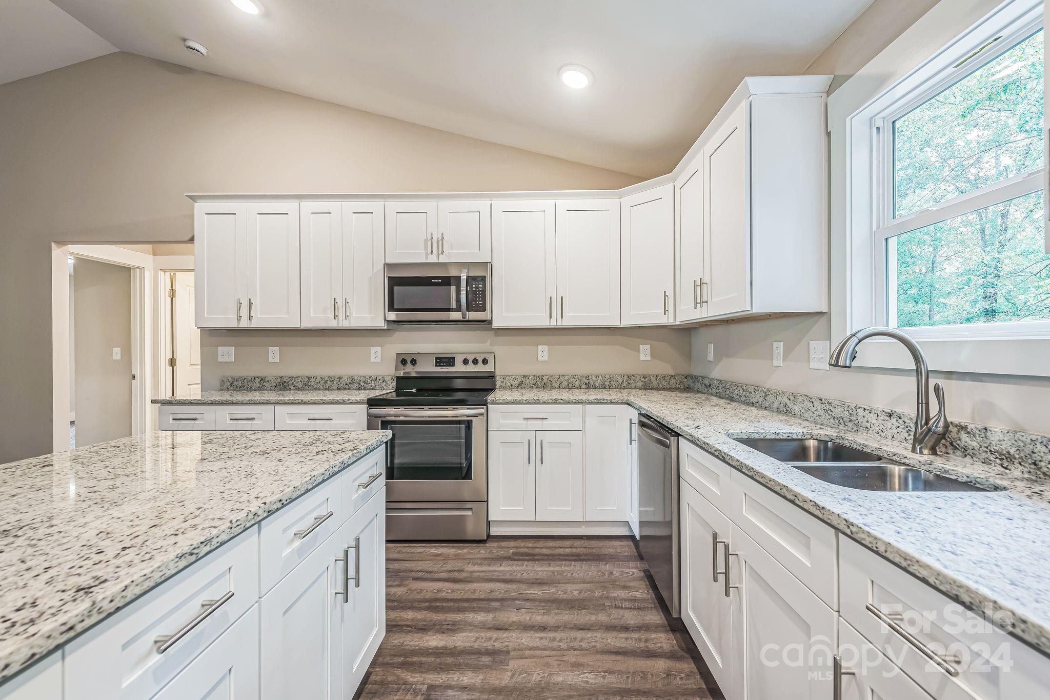 a kitchen with kitchen island granite countertop white cabinets white appliances a sink and a window