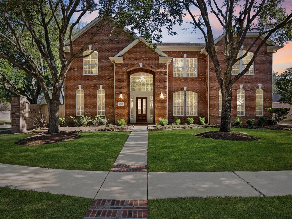 This two-story brick home boasts large windows, a welcoming entrance, and a beautifully maintained front yard adorned with mature trees.