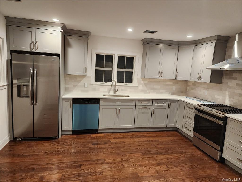 Kitchen with dark hardwood / wood-style floors, stainless steel appliances, gray cabinetry, sink, and wall chimney range hood