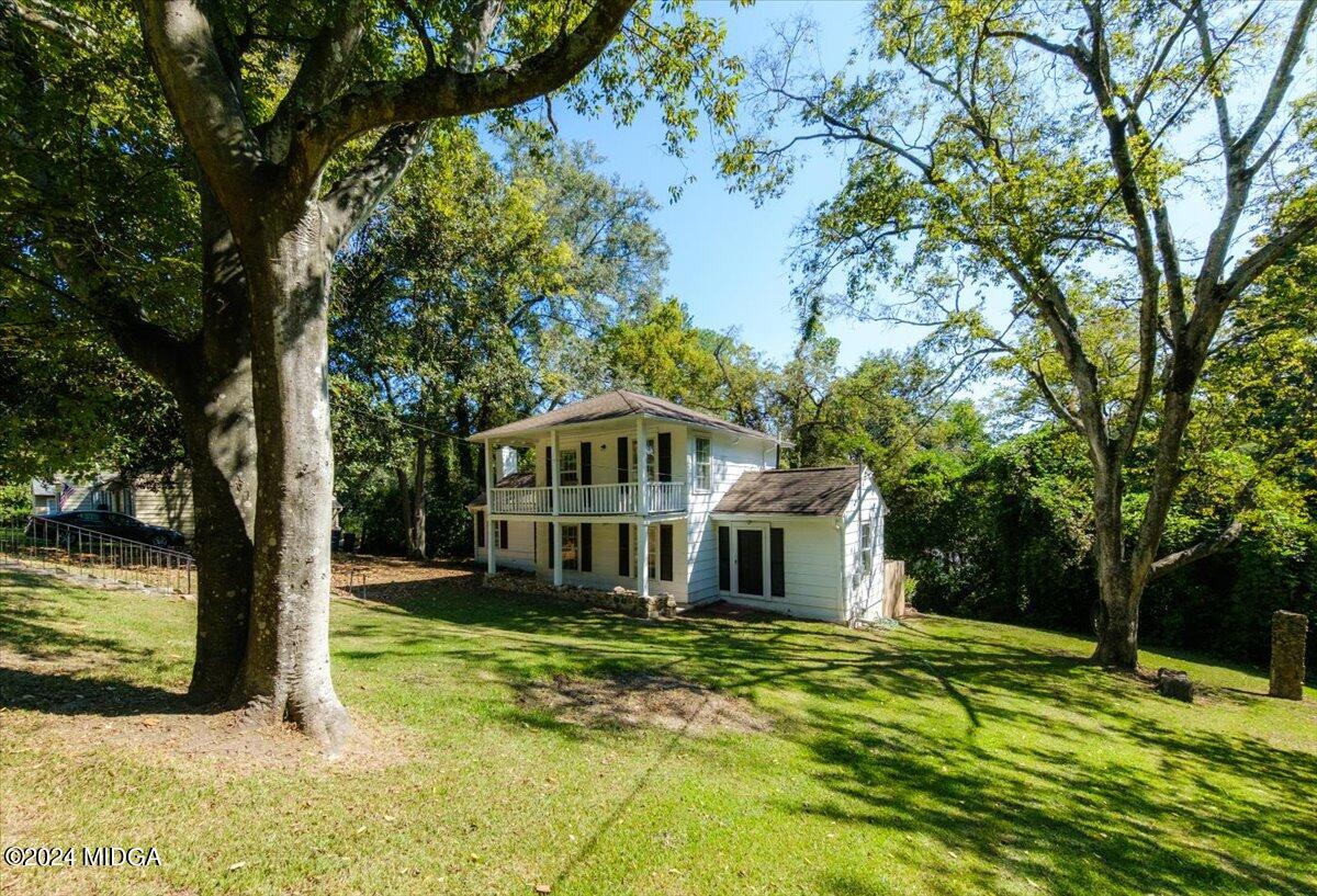 a white house with a big yard plants and large trees