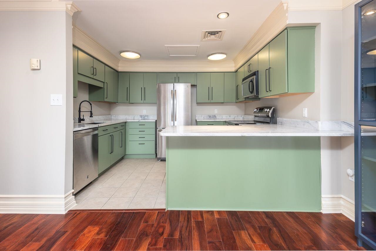 Kitchen with sink, kitchen peninsula, green cabinetry, appliances with stainless steel finishes, and wood-type flooring