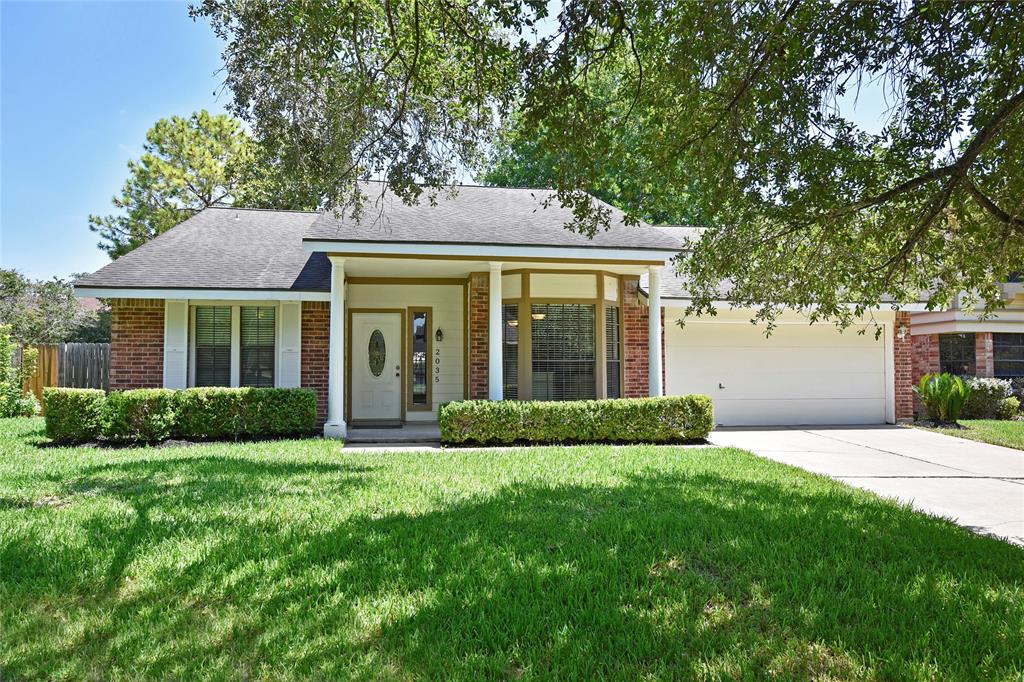 a view of house in front of a yard with potted plants and large trees