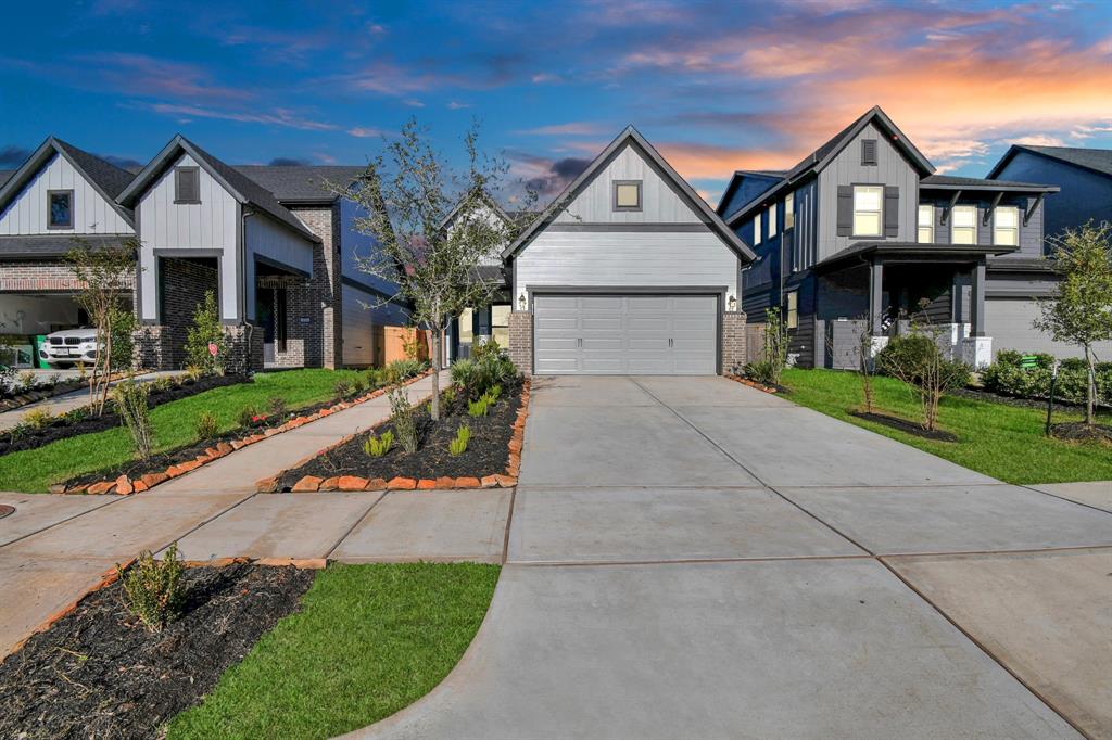 This photo showcases a modern, single-family home with a two-car garage, well-maintained landscaping, and a spacious driveway. The neighborhood appears tidy and upscale, with similar homes lining the street. The sky is beautifully lit, adding to the home's curb appeal.