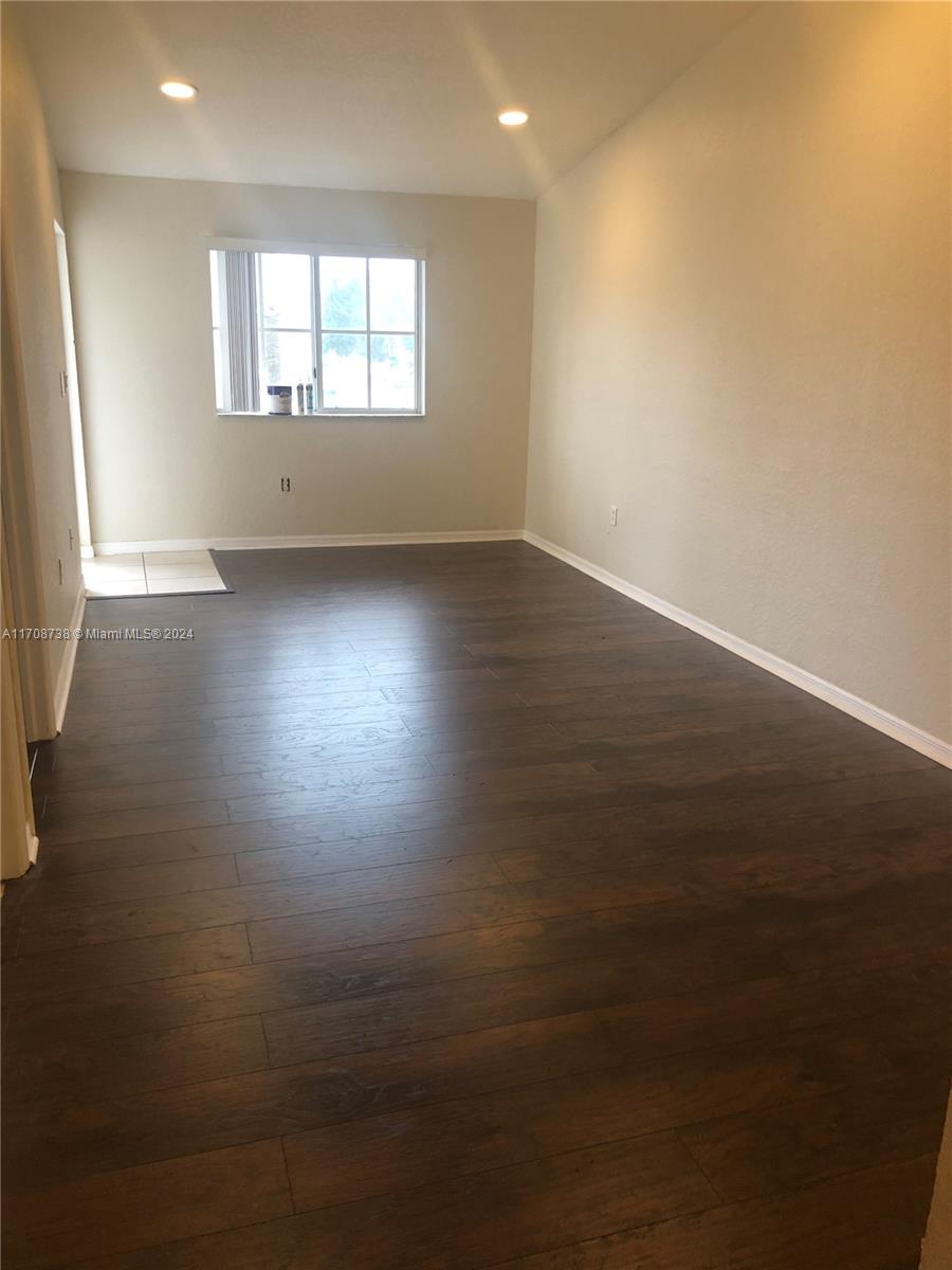 an empty room with wooden floor and windows with curtains