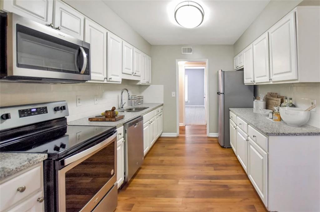 a kitchen with granite countertop a stove top oven a sink dishwasher and white cabinets with wooden floor