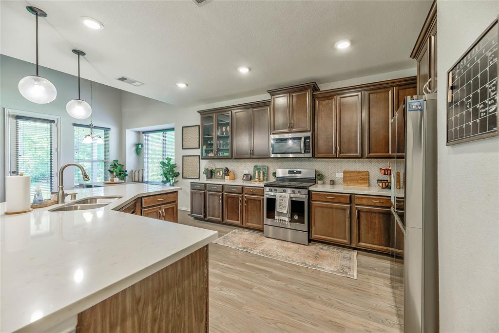 a kitchen with stainless steel appliances granite countertop a stove top oven a sink dishwasher a refrigerator and a dining table with wooden floor