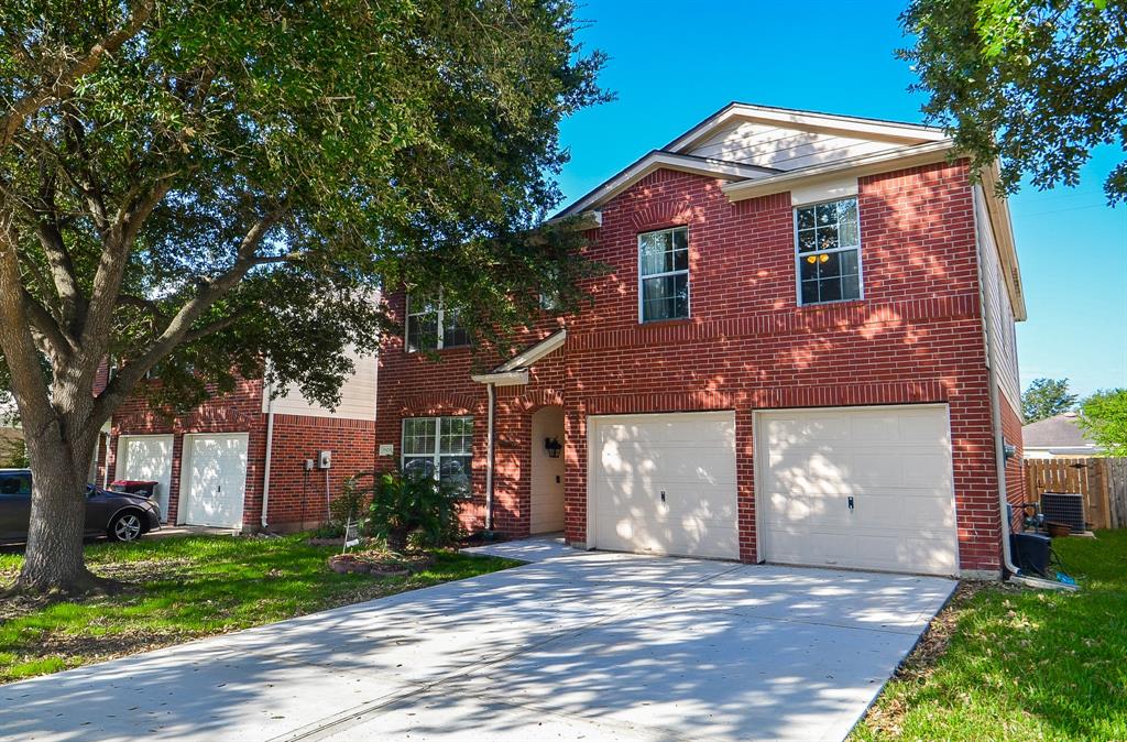 This is a two-story brick home featuring a double garage, large windows, and mature trees in the front yard, offering both curb appeal and shade.