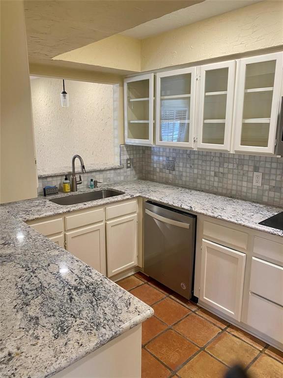 Kitchen with sink, backsplash, dishwasher, and light stone counters