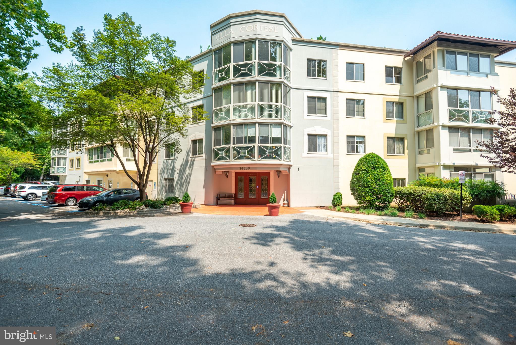 a front view of a building with lot of cars and trees