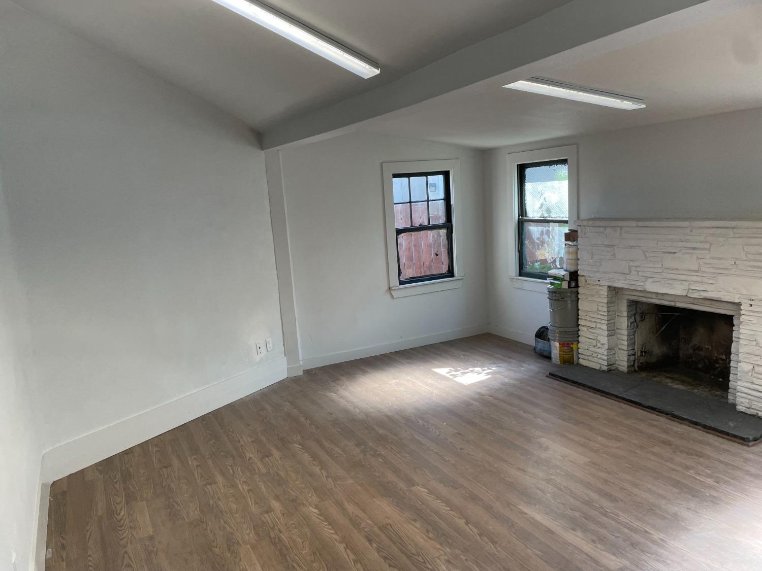 an empty room with wooden floor fireplace and windows