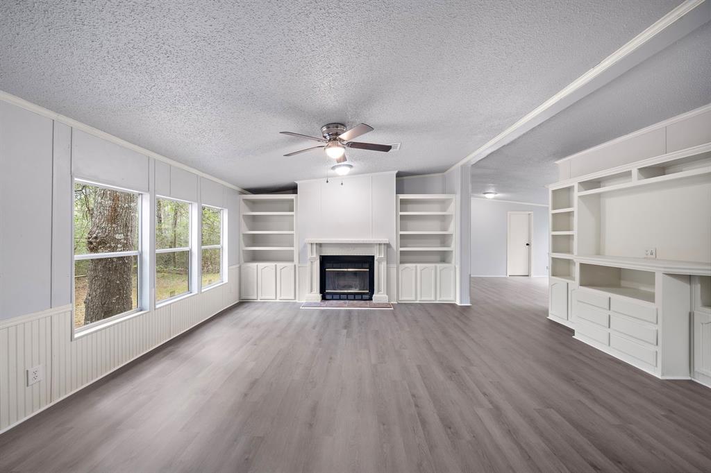 a view of an empty room with wooden floor fireplace and a window